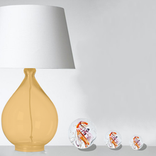 Load image into Gallery viewer, Photo d&#39;ambiance, mise en situation de 3 sulfures presses papiers modèle cyclone multicolore à coté d&#39;une lampe de chevet. 
